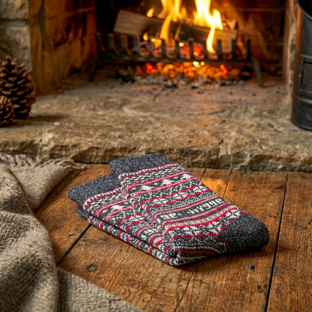 Folded pairs of charcoal Fair Isle Swoollies merino wool socks neatly arranged on the floor in front of a fireplace